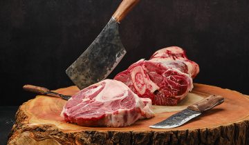 Big hunk of beef partly cut on a cutting board with knives